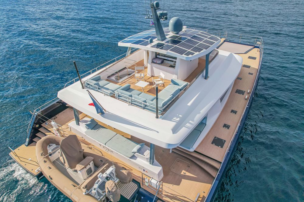 Modern luxury yacht with solar panels and tender boat cruising on blue water.