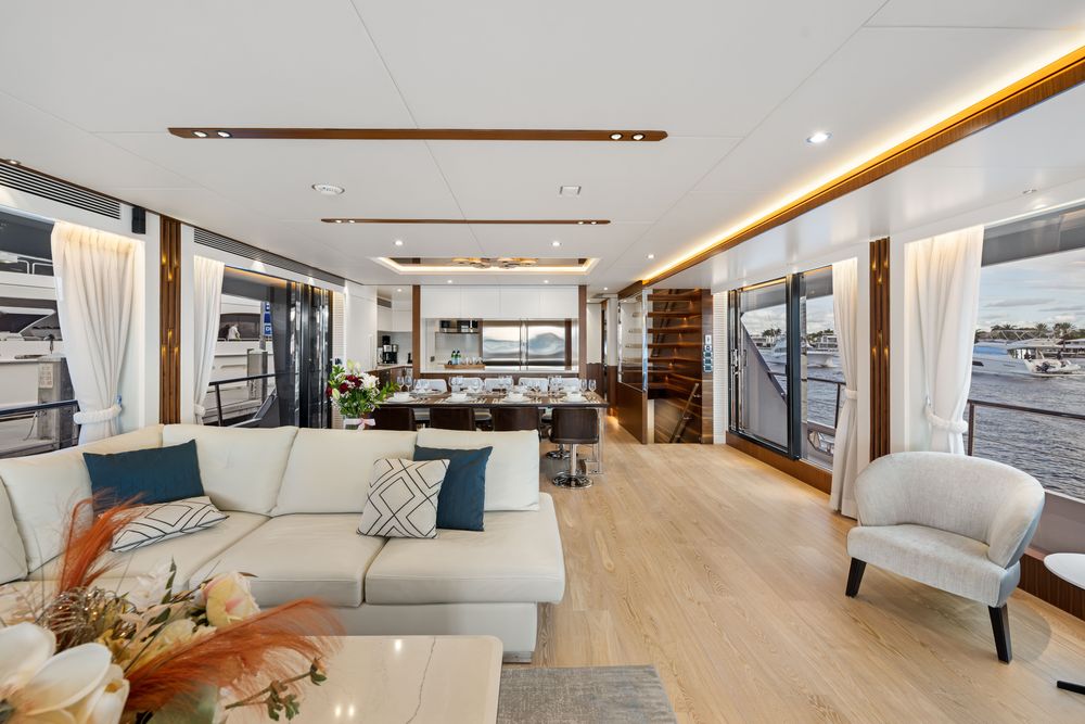 Modern yacht interior with white sofa, dining area, and large windows overlooking water.