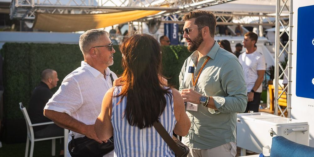 Three attendees, two men and a woman, networking and conversing at an outdoor event.