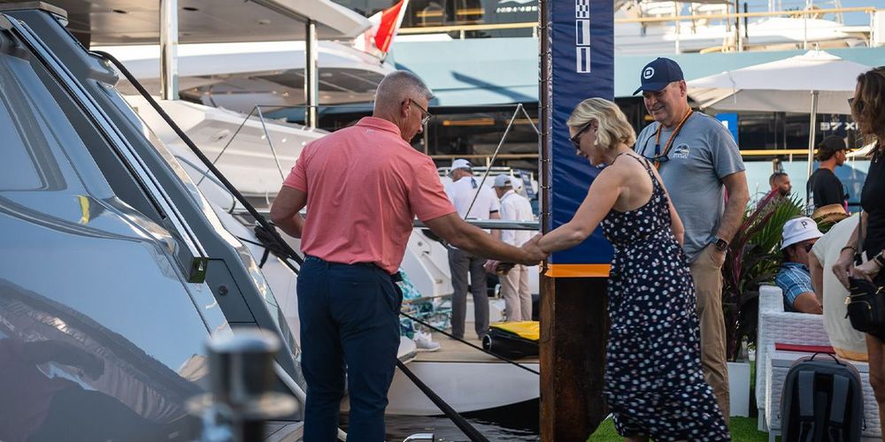 Man in pink shirt shakes hands with woman in floral dress at a boat show.