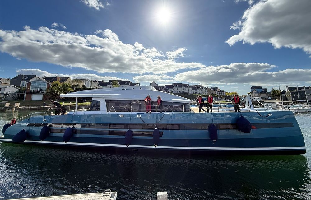 A large blue and white catamaran docked with people on deck under a sunny sky.