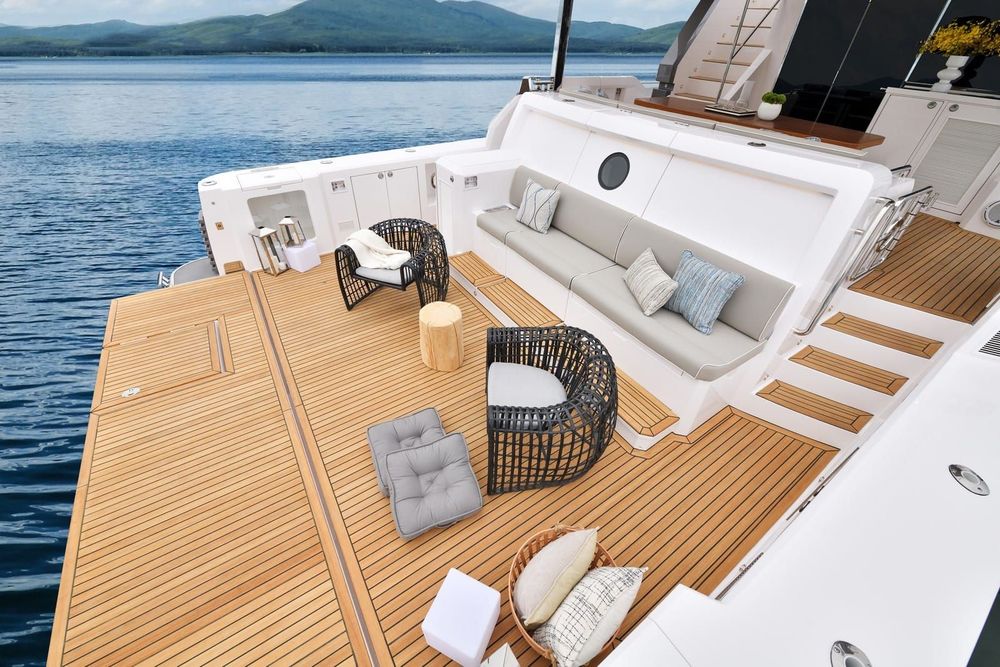 A yacht's aft deck features comfortable outdoor seating, with ocean and mountains in the background.