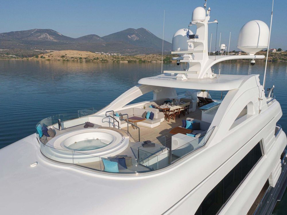 White luxury yacht deck with hot tub, lounge, and dining area on calm water.