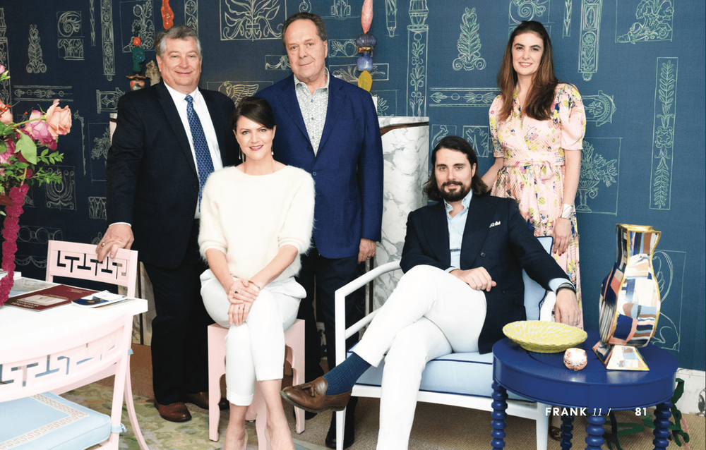 Five people, three men and two women, pose in a stylish blue room with patterned walls.