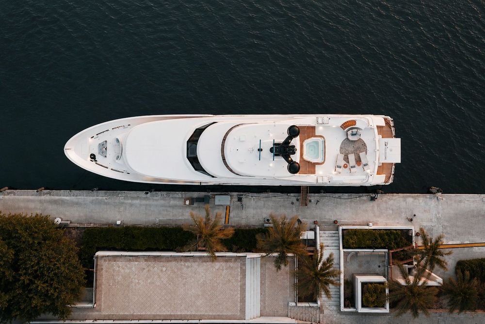 Aerial view of a white luxury yacht with brown deck details docked at a pier.