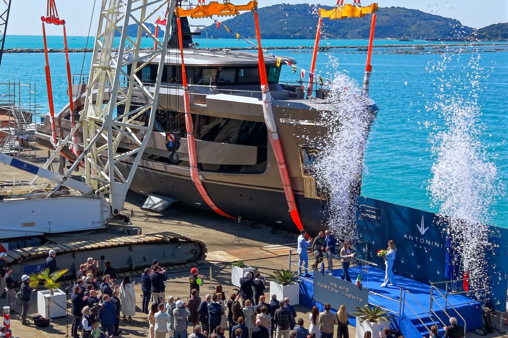 Luxury yacht launched into blue water by a crane with a celebratory crowd.