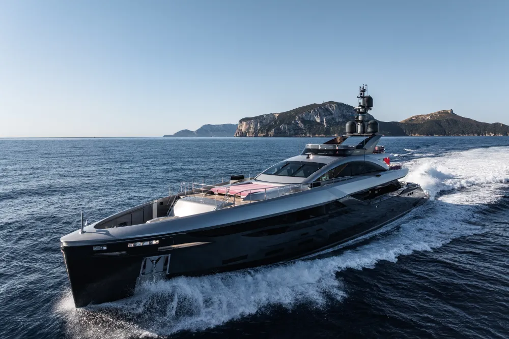Dark, sleek superyacht speeding across blue ocean water, creating a white wake.