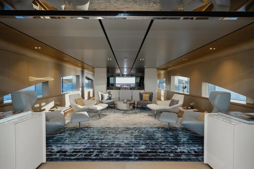 Spacious, modern yacht lounge with luxurious cream seating, patterned rug, and bright windows.
