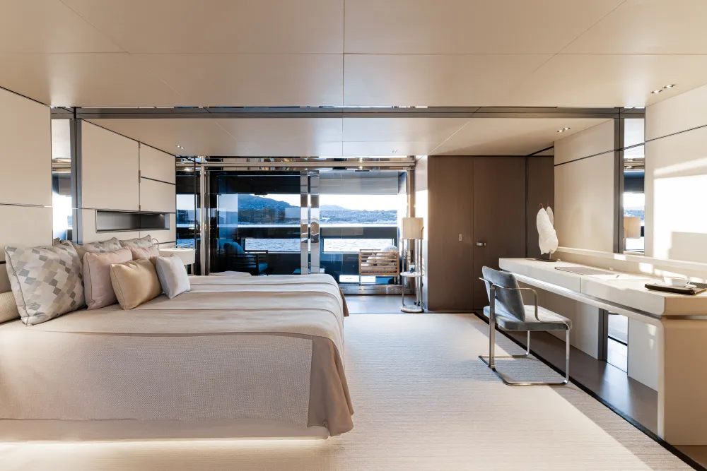 Luxurious modern yacht bedroom featuring a large bed, desk, and scenic water view.