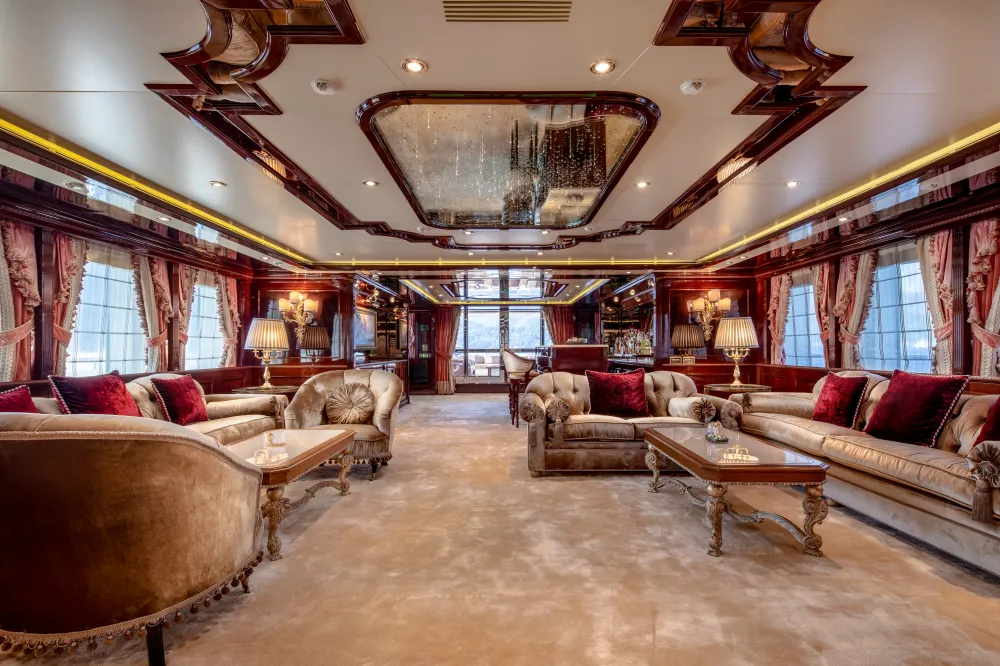 Luxurious salon with ornate sofas, red curtains, wooden ceiling, and large windows.