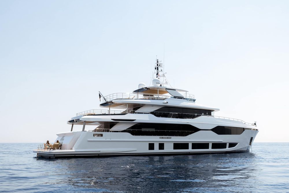 A large white luxury yacht with multiple decks sails on calm blue ocean water.