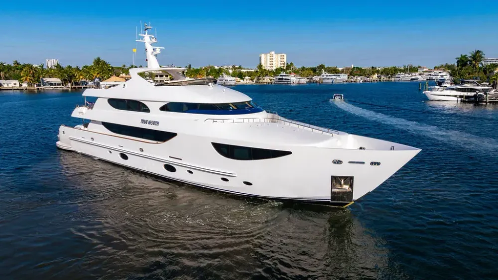 Large white luxury yacht cruising on a blue waterway under a clear sky.