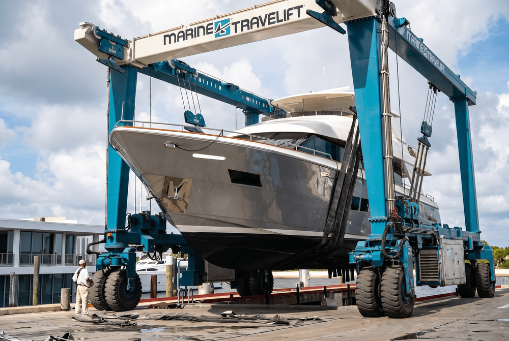 A large grey yacht is lifted by a blue Marine Travelift crane.