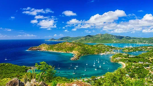 Aerial view of a vibrant tropical bay with green hills, turquoise water, and anchored sailboats.