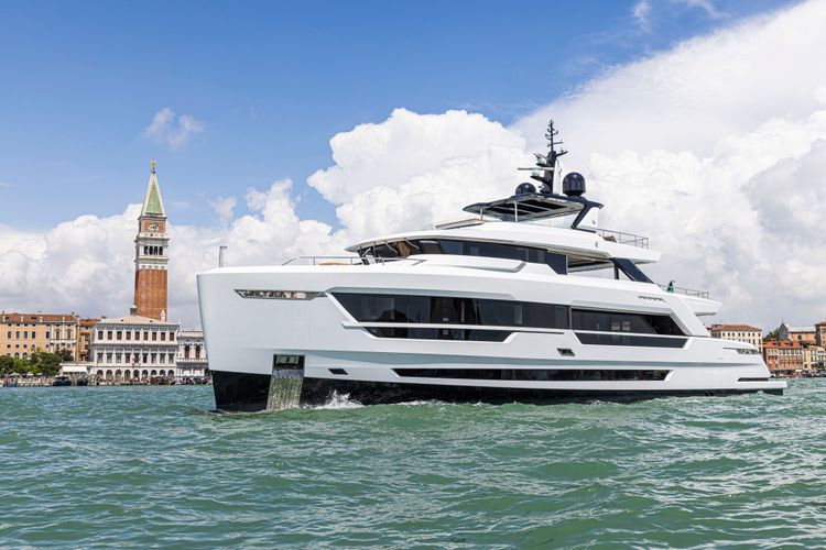 White luxury yacht sailing on a canal in Venice with a historic bell tower.