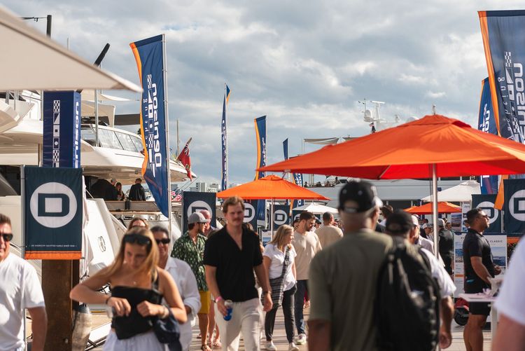 Crowd of people walking among yachts and exhibition banners at a lively boat show.