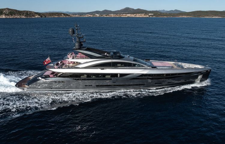A sleek, modern superyacht with a dark hull cruises across deep blue water near distant land.