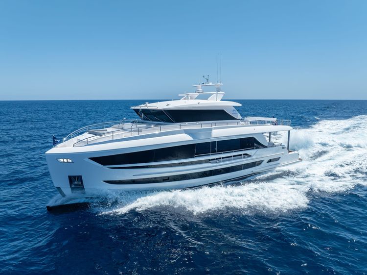 A sleek white luxury yacht cruises across a calm blue ocean under a clear sky.