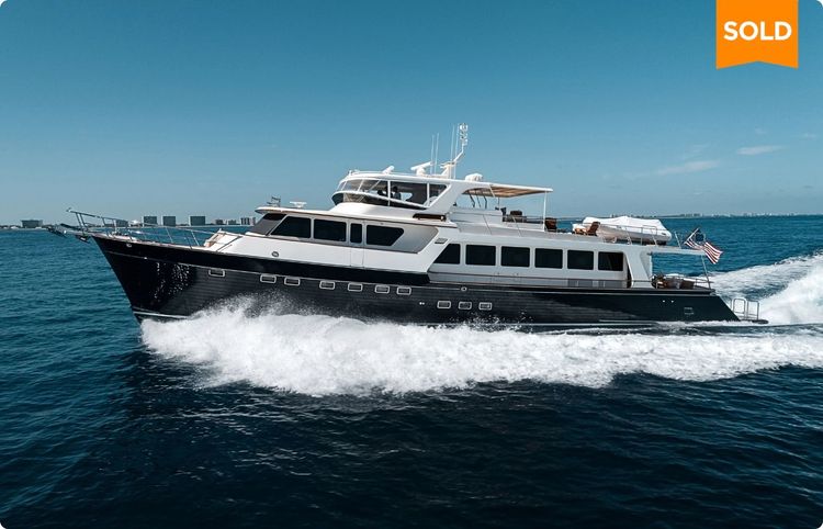 Large, sold motor yacht with dark hull speeding across blue water.