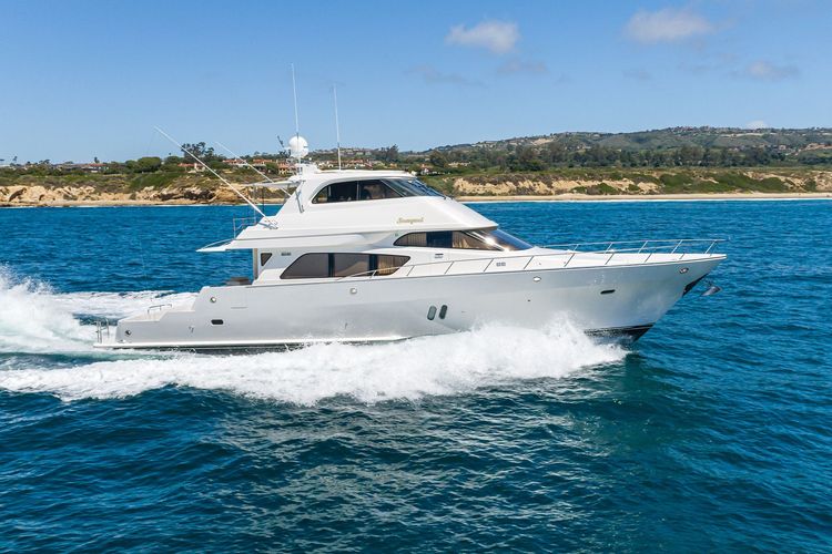 Large white motor yacht cruising swiftly on blue ocean water near a green coastline.
