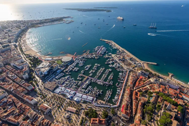 Coastal city marina filled with yachts, beach, and urban landscape from above.