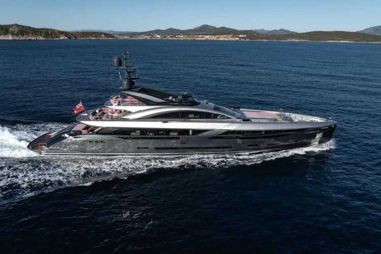 A sleek, modern silver superyacht cruises quickly across calm blue ocean water.