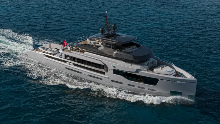 A sleek grey and black yacht cruises across clear blue water, leaving a white wake.