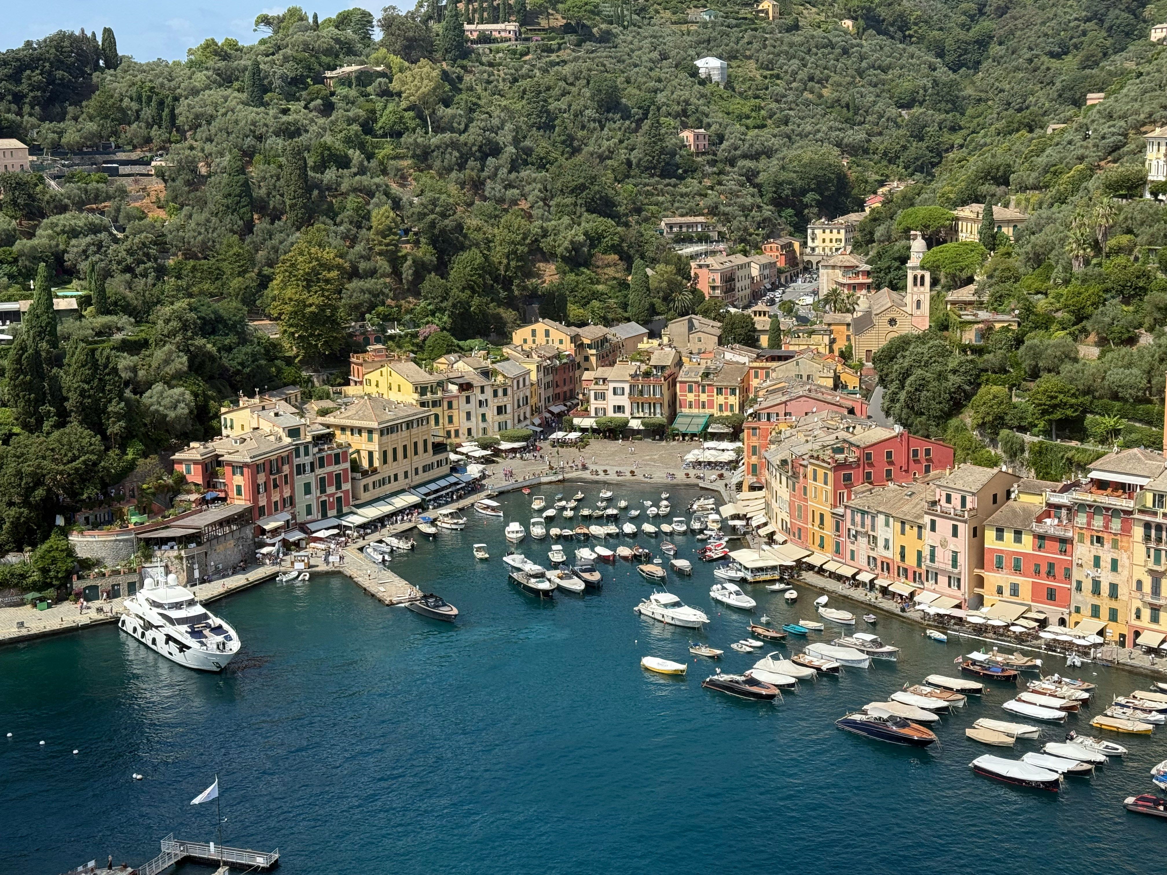 Colorful coastal town with a vibrant harbor, many boats, and lush green hills.