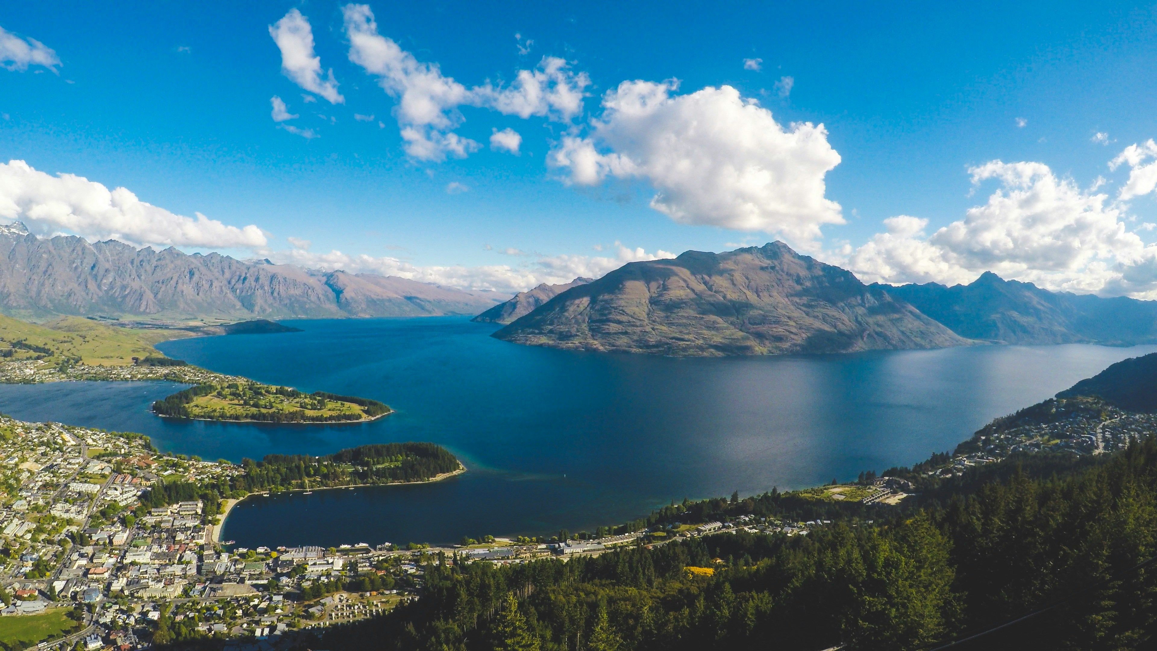Panoramic view of a scenic lake, majestic mountains, and a vibrant lakeside town under a blue sky.