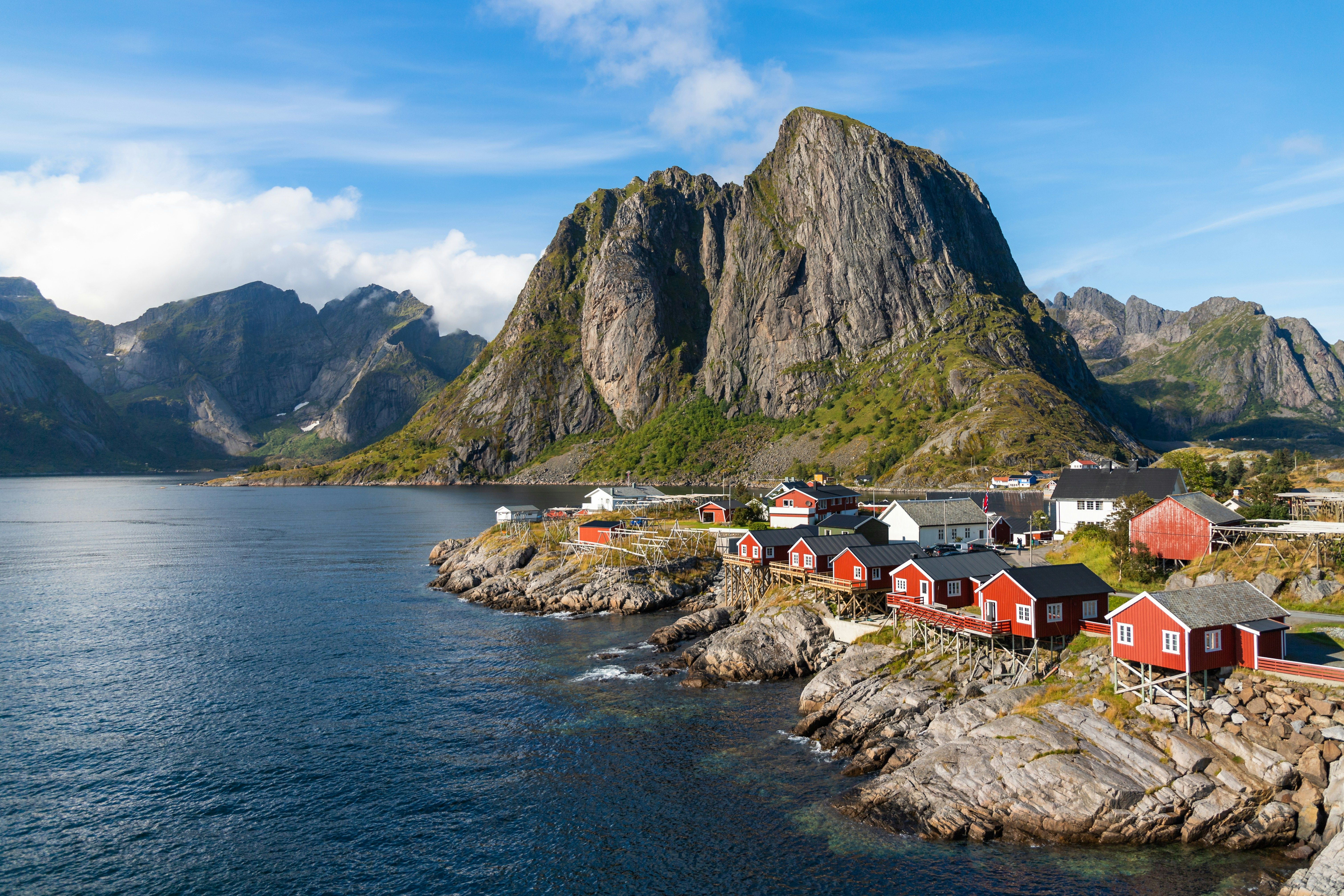 Coastal village with red houses nestled by a large mountain and clear blue water.