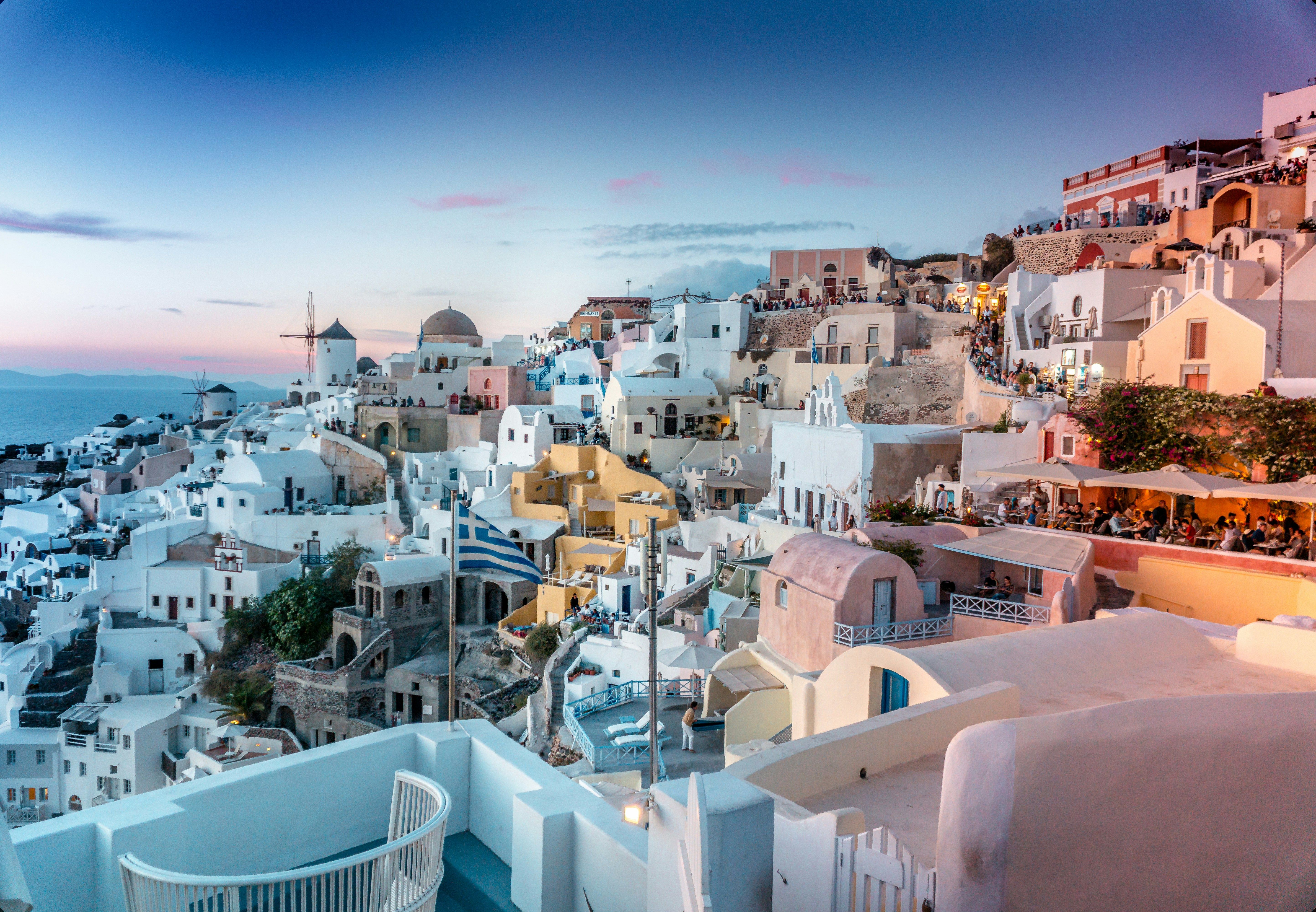 Panoramic view of white buildings in Oia, Santorini, overlooking the Aegean Sea at dusk.