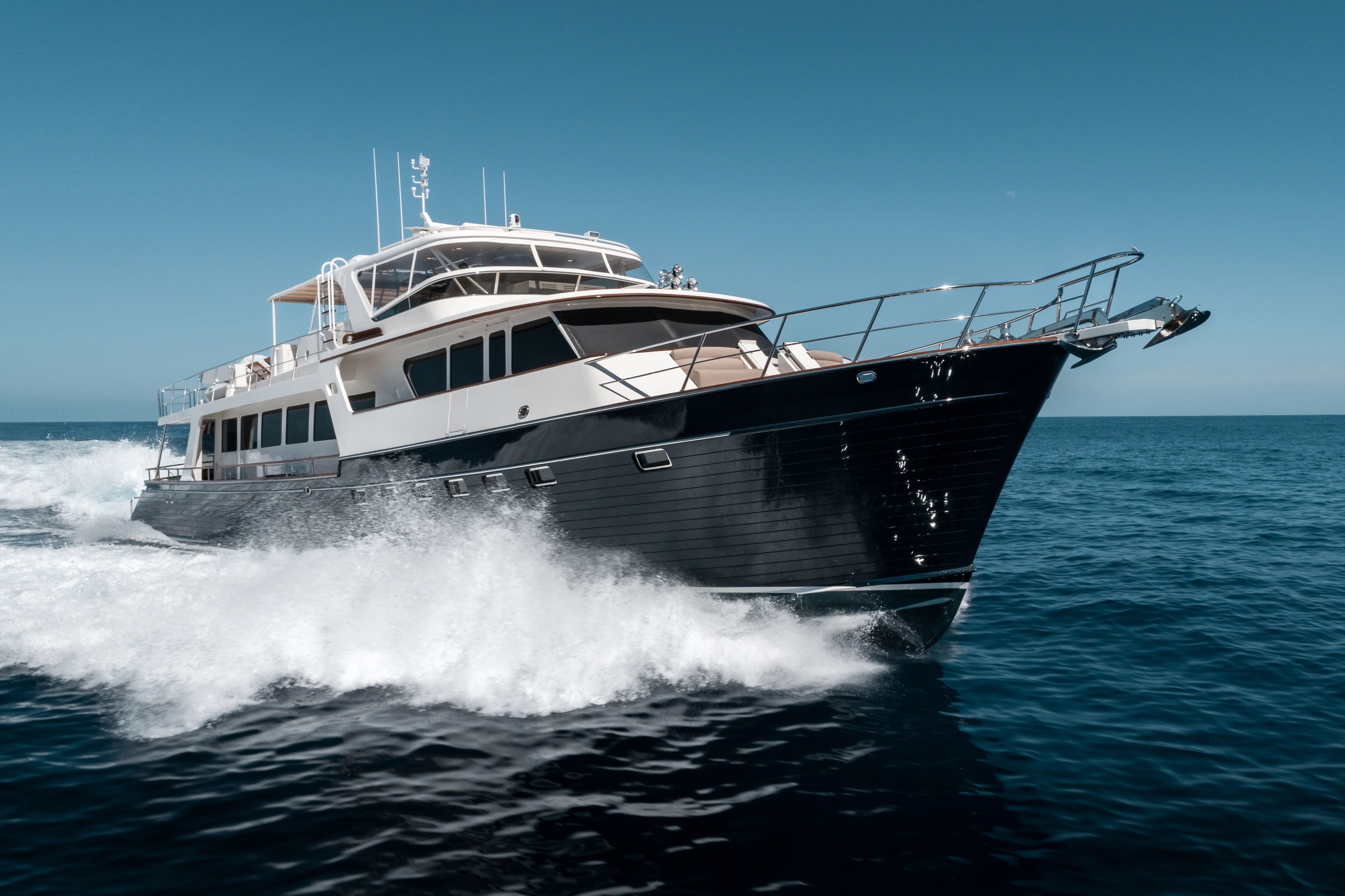 Large dark blue and white yacht speeding across blue ocean, leaving a white wake.