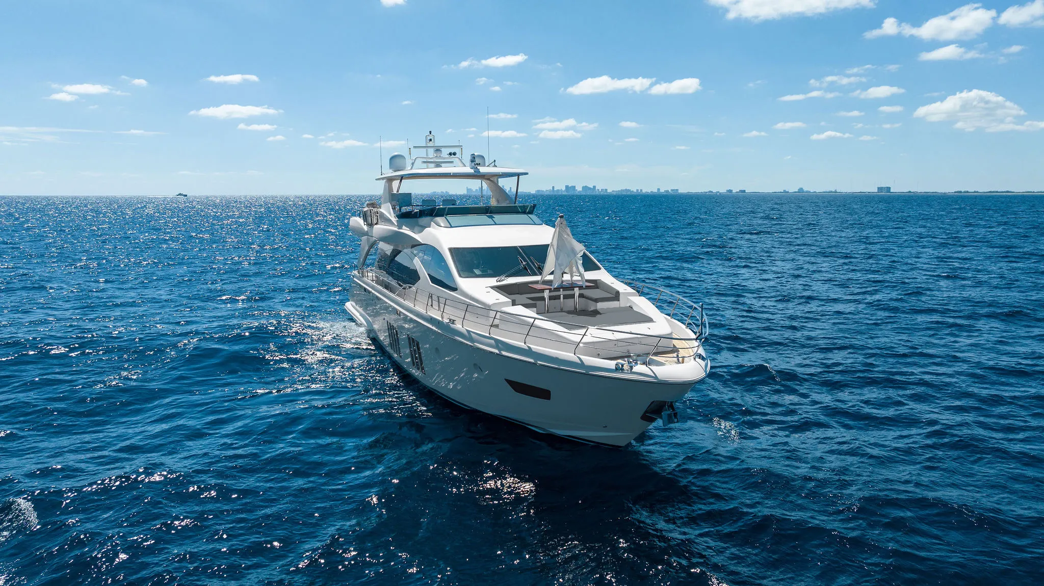 A white luxury yacht cruises on deep blue ocean water under a clear sky.
