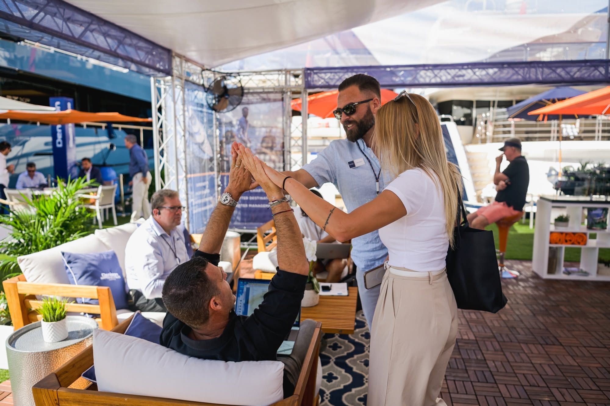 Three people at an outdoor event high-fiving and smiling under a white tent.