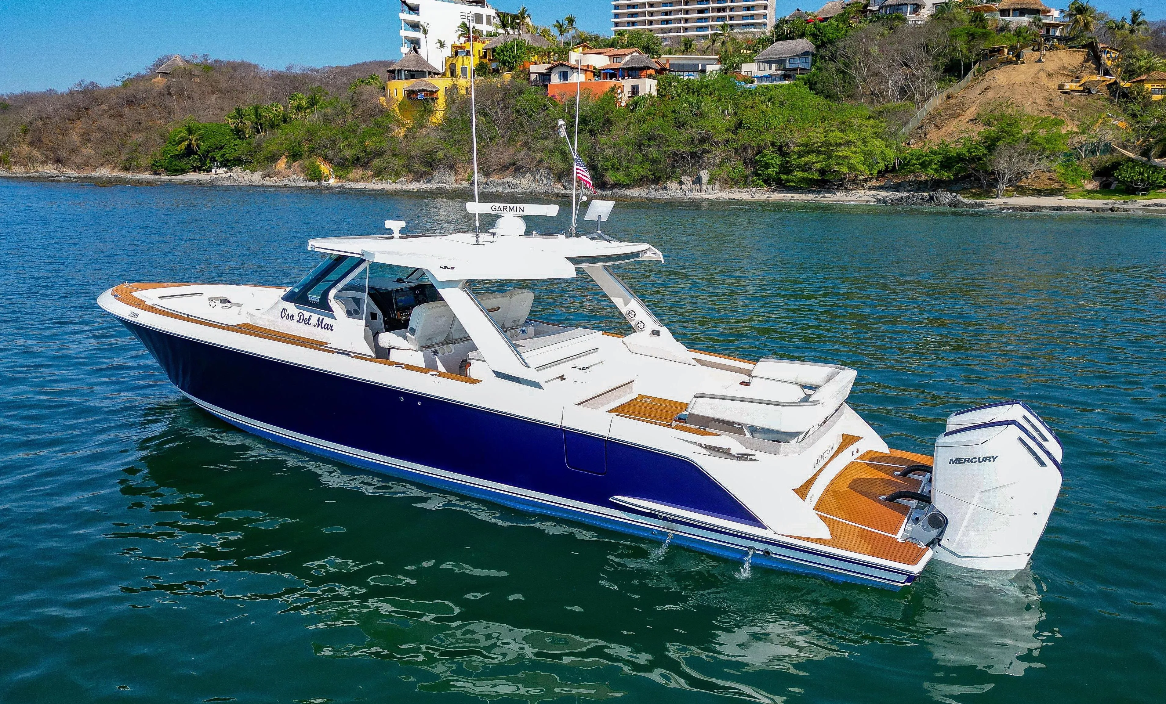 Blue and white motor yacht with outboard engines cruising in calm tropical waters.
