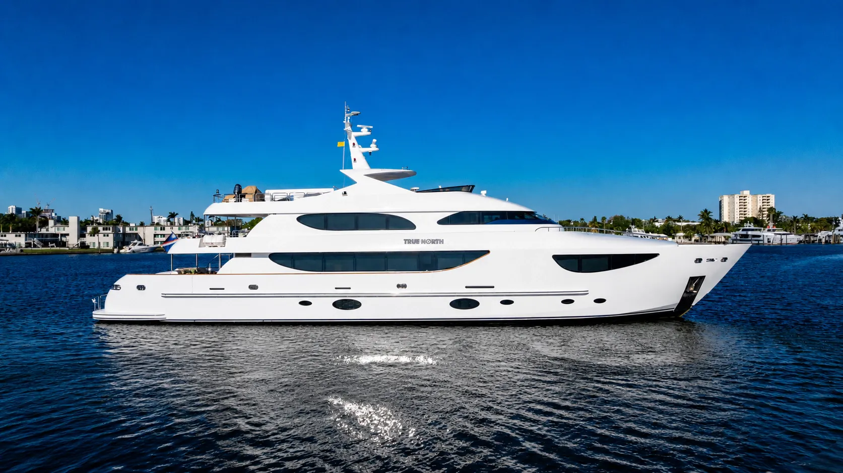 A sleek white luxury yacht cruises on calm blue water under a clear sky.