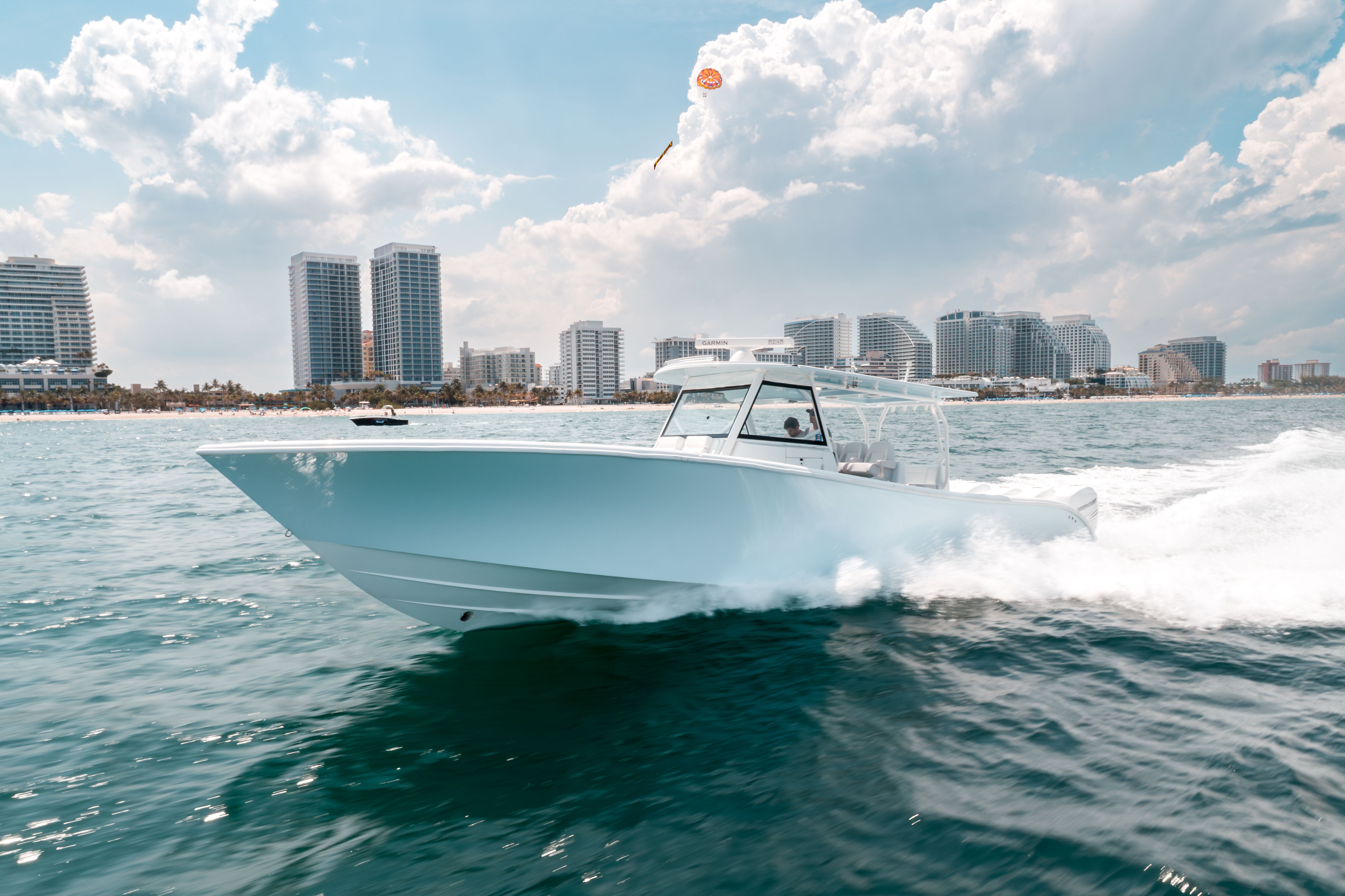 Light blue motorboat creating a wake speeds across water with a coastal city skyline.