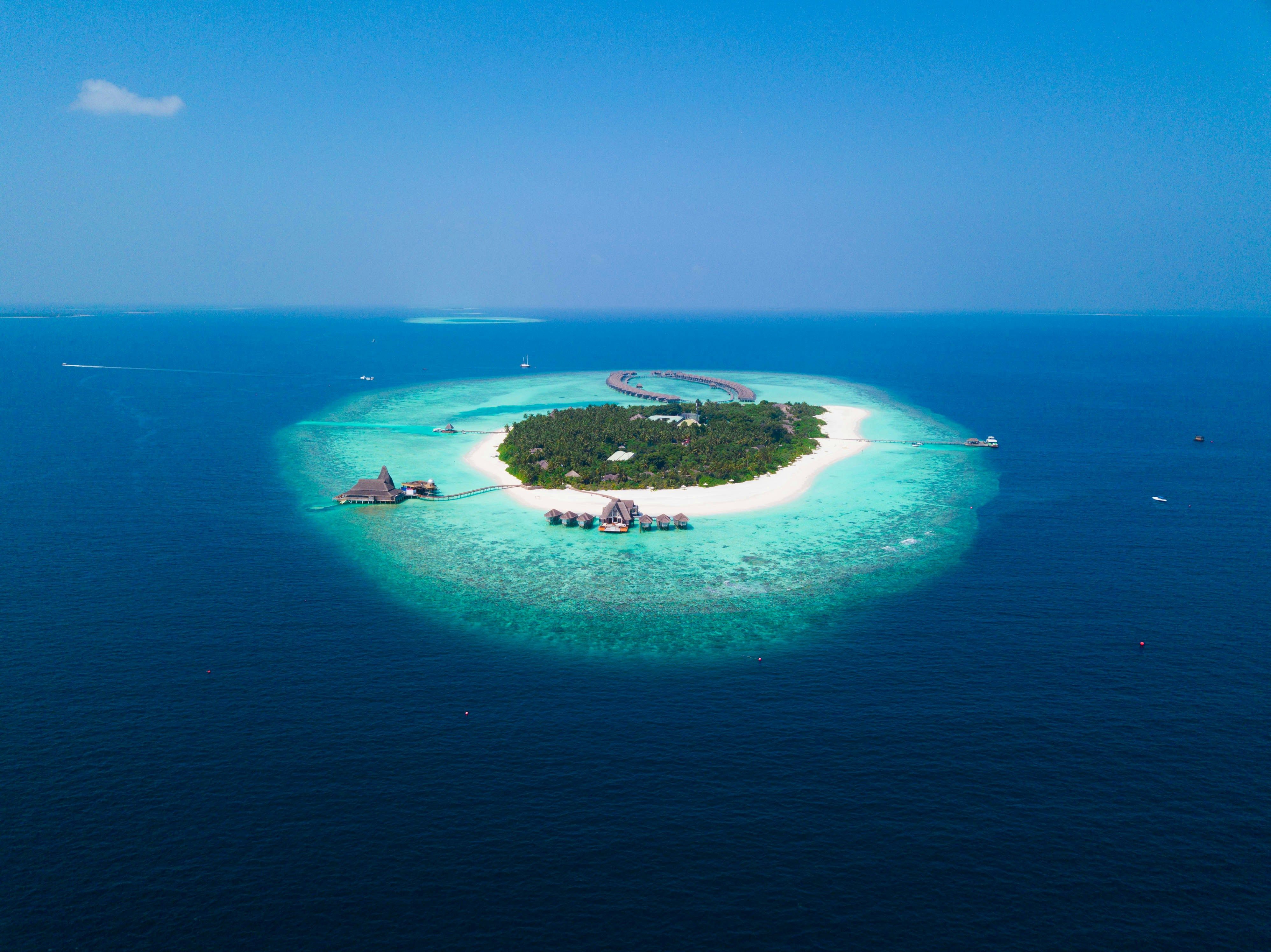 Aerial view of a tropical island with white sand, palm trees, and overwater bungalows.